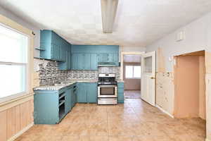 Kitchen featuring blue cabinets, sink, light tile patterned floors, stainless steel range with gas cooktop, and backsplash