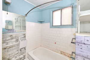 Bathroom featuring crown molding, bathtub / shower combination, and tile walls