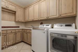 Clothes washing area featuring washer and dryer, light tile patterned flooring, sink, and cabinets