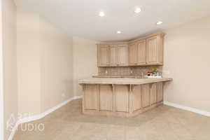 Kitchen with tile countertops, sink, backsplash, kitchen peninsula, and light brown cabinets