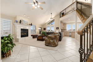 Tiled living room featuring ceiling fan, high vaulted ceiling, and a high end fireplace