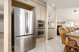 Kitchen featuring ceiling fan, appliances with stainless steel finishes, a tile fireplace, and light tile patterned floors