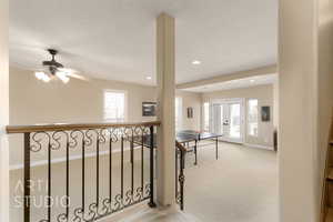 Corridor featuring light carpet, a wealth of natural light, french doors, and a textured ceiling