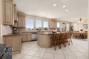 Kitchen featuring dishwasher, backsplash, a kitchen breakfast bar, light tile patterned floors, and light brown cabinets