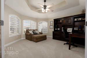 Office area with ceiling fan, a raised ceiling, and light carpet