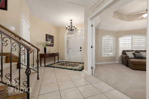 Foyer with light colored carpet and ceiling fan with notable chandelier