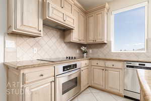 Kitchen featuring light tile patterned flooring, backsplash, custom exhaust hood, light stone counters, and stainless steel appliances