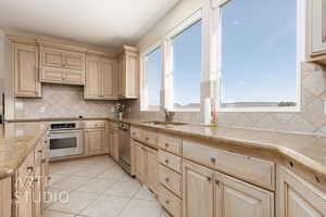 Kitchen with sink, light tile patterned floors, appliances with stainless steel finishes, tasteful backsplash, and light brown cabinetry