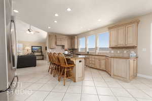 Kitchen with light tile patterned flooring, a kitchen island, stainless steel fridge, and a breakfast bar area