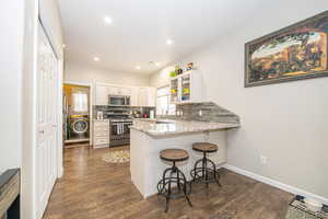 Kitchen featuring a breakfast bar, stainless steel appliances, decorative backsplash, washer / dryer, and kitchen peninsula