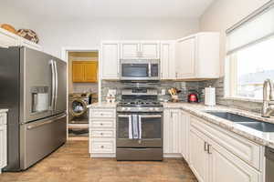 Kitchen with white cabinetry, washing machine and clothes dryer, stainless steel appliances, and sink