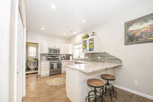 Kitchen featuring appliances with stainless steel finishes, white cabinetry, washer / dryer, backsplash, and a kitchen breakfast bar