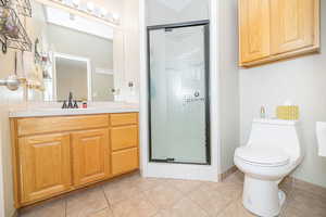 Bathroom featuring vanity, a shower with shower door, tile patterned floors, and toilet