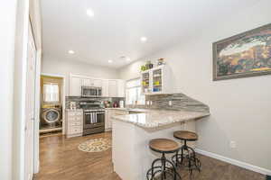 Kitchen featuring a breakfast bar area, white cabinetry, stainless steel appliances, washer / dryer, and kitchen peninsula