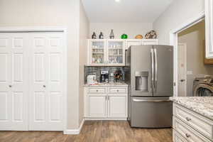 Kitchen featuring washer / clothes dryer, light stone countertops, white cabinets, and stainless steel fridge