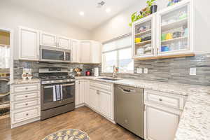 Kitchen with sink, appliances with stainless steel finishes, hardwood / wood-style flooring, light stone countertops, and white cabinets