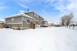 Snow covered back of property with central air condition unit and a pergola