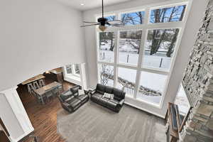 Living room featuring ceiling fan, plenty of natural light, a stone fireplace, and dark wood-type flooring