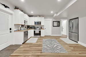 Kitchen featuring white cabinetry, sink, stainless steel appliances, and butcher block countertops