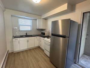 Unit 1 Kitchen with sink, white appliances, a baseboard heating unit, white cabinets, and decorative backsplash