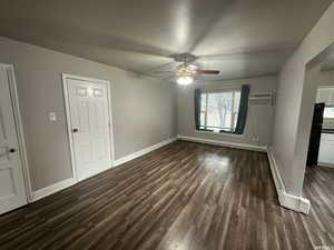 Unit 3  family room with dark wood-type flooring, a baseboard radiator, ceiling fan, and a wall unit AC