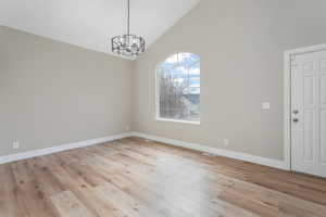 Unfurnished dining area with an inviting chandelier, high vaulted ceiling, and light hardwood / wood-style floors