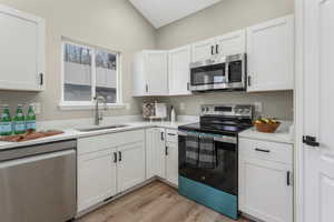 Kitchen featuring white cabinetry, stainless steel appliances, sink, and light wood-type flooring