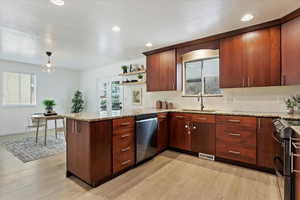 Kitchen featuring sink, kitchen peninsula, stainless steel appliances, light stone countertops, and light wood-type flooring