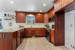 Kitchen featuring stainless steel appliances, light stone countertops, sink, and light wood-type flooring