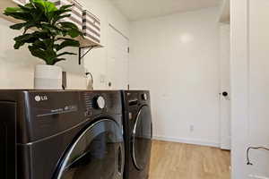 Washroom with separate washer and dryer and light wood-type flooring