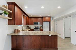 Kitchen with sink, light hardwood / wood-style flooring, stainless steel appliances, light stone counters, and kitchen peninsula