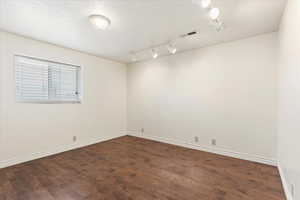 Empty room featuring dark wood-type flooring, rail lighting, and a textured ceiling