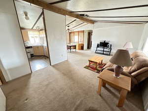 Living room featuring light carpet, vaulted ceiling with beams, and a textured ceiling