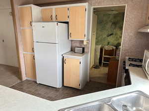 Kitchen with light brown cabinets, gas stove, white fridge, and dark tile patterned floors