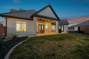 Back house at dusk featuring ceiling fan, a yard, a hot tub, and a patio area