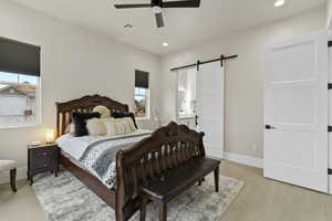 Bedroom 2 with ensuite bath, light hardwood / wood-style floors, a barn door, and ceiling fan