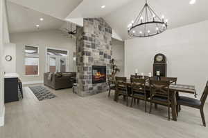 Dining space with ceiling fan, a fireplace, high vaulted ceiling, and light hardwood / wood-style flooring