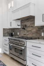 Kitchen with custom exhaust hood, white cabinetry, tasteful backsplash, light stone countertops, and range with two ovens