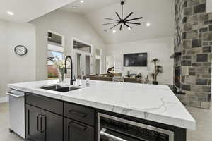 Kitchen featuring sink, a fireplace, light stone countertops, and a center island with sink