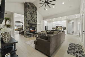 Living room with a stone fireplace, light wood-type flooring, a notable chandelier, and high vaulted ceiling