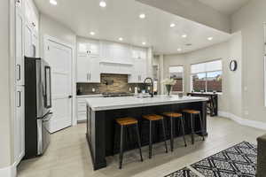 Kitchen with a breakfast bar, high end fridge, sink, a center island with sink, and white cabinets