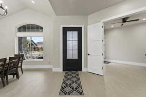 Foyer featuring vaulted ceiling, ceiling fan with notable chandelier, and light wood-type flooring