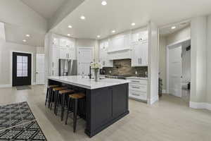 Kitchen with light stone counters, high end refrigerator, an island with sink, and white cabinets