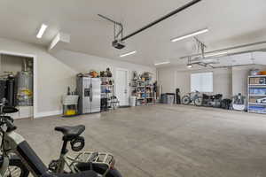 Garage with stainless steel refrigerator with ice dispenser, a garage door opener, and water heater