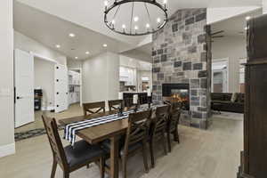 Dining room featuring lofted ceiling, light wood-type flooring, a chandelier, and a fireplace