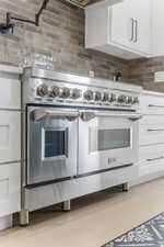 Kitchen with double oven range, decorative backsplash, white cabinets, and light wood-type flooring