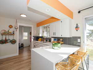 Kitchen featuring a breakfast bar, sink, kitchen peninsula, decorative backsplash, and white cabinets