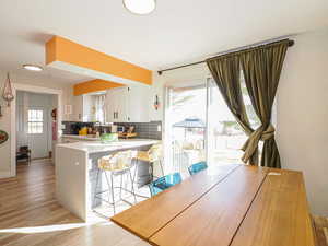 Kitchen featuring a breakfast bar, white cabinetry, light hardwood / wood-style flooring, kitchen peninsula, and backsplash