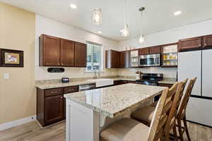 Kitchen featuring a kitchen island, appliances with stainless steel finishes, pendant lighting, sink, and light stone countertops