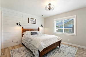 Bedroom featuring a textured ceiling, light hardwood / wood-style floors, and wood walls